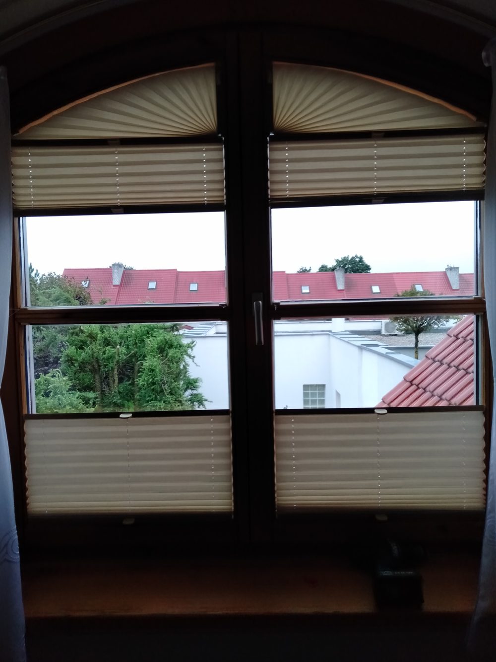 Okno łukowe z widokiem na dachy, plisy w dolnych kwaterach